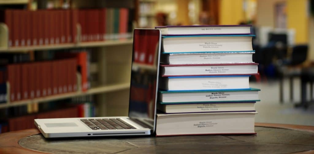 Photograph of a laptop along with a stack of books